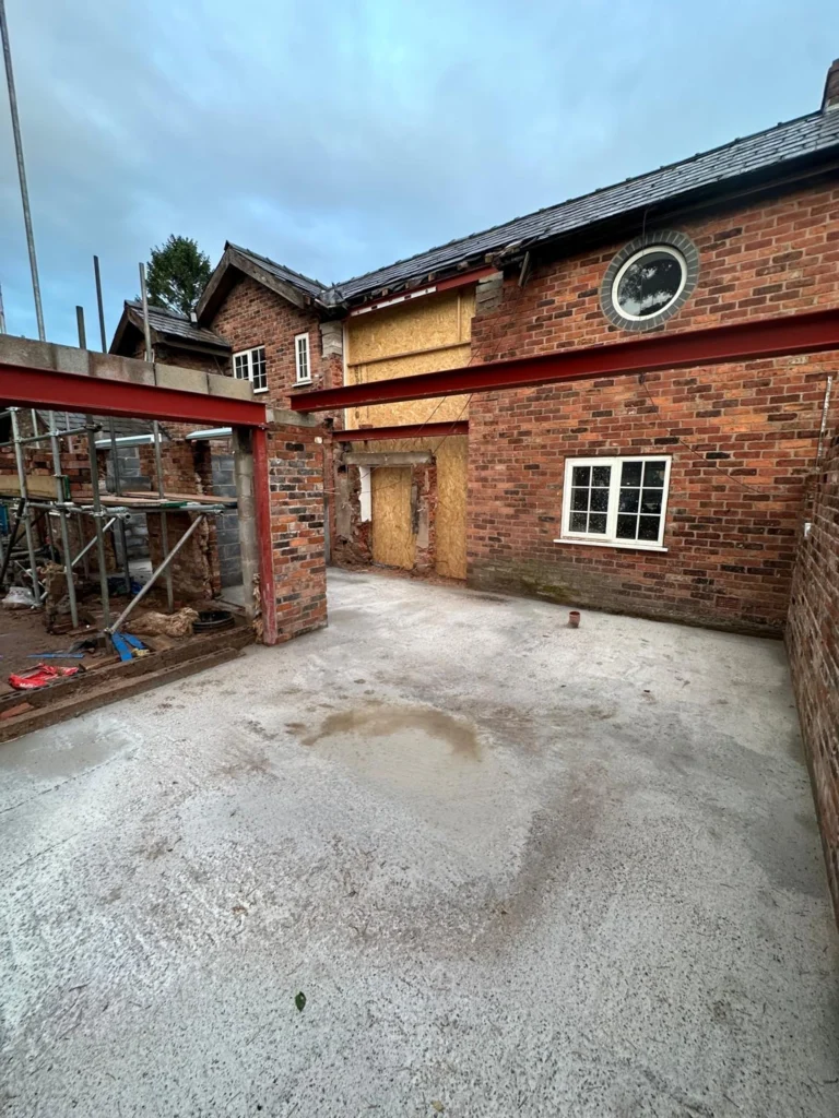 A red brick house under renovation with a new concrete floor, scaffolding, and structural steel RSJ beams.